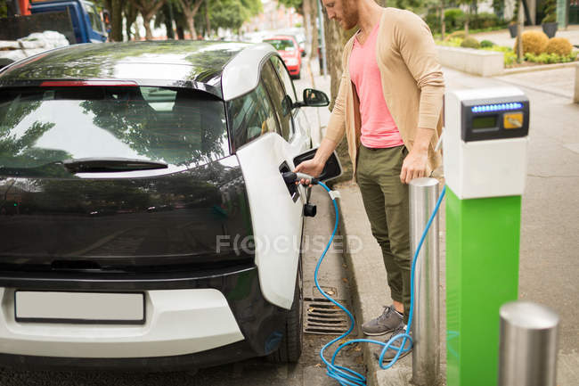 Умный человек заряжает электромобиль на зарядной станции — стоковое фото