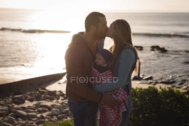 Пара цілується і тримає дитину між ними на пляжі — стокове фото