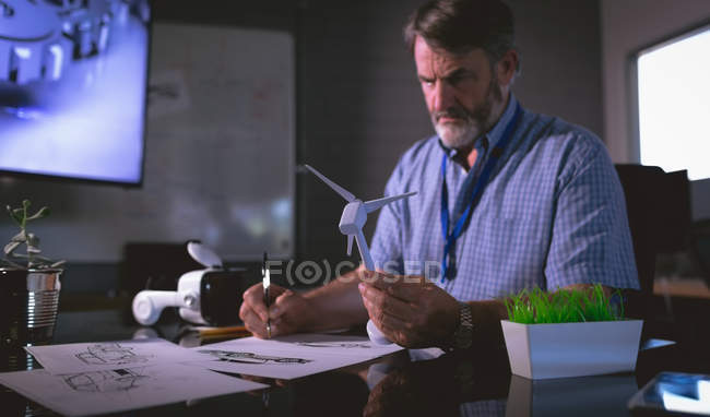 Homme cadre examinant un modèle de moulin à vent dans le bureau — Photo de stock