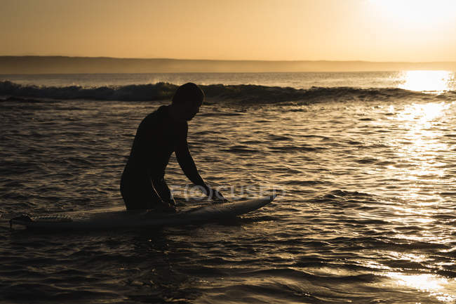 Surfista con tabla de surf surfeando en el mar al atardecer - foto de stock