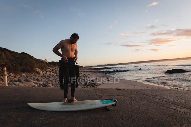 Surfista vestindo traje na praia durante o pôr do sol — Fotografia de Stock