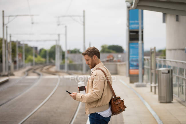 Розумний чоловік використовує мобільний телефон на платформі на залізничному вокзалі — стокове фото