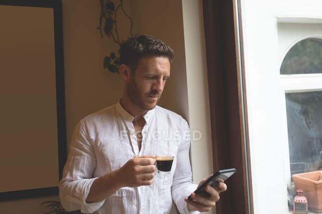 Чоловік використовує мобільний телефон, маючи чорну каву вдома — стокове фото