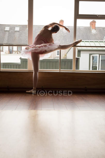 Задний вид балерины, практикующей балет у окна в танцевальной студии — стоковое фото