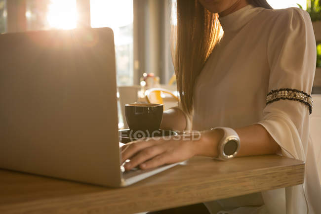 Средняя часть женщины, использующей ноутбук в кафе — стоковое фото