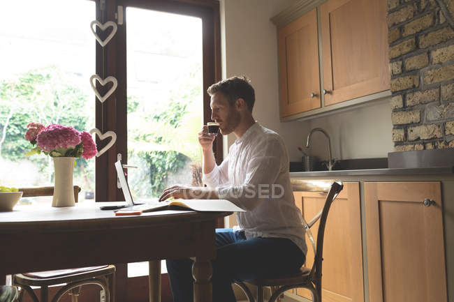 Мужчина пьет кофе дома, пользуясь ноутбуком — стоковое фото