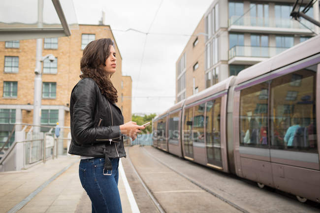 Красивая женщина с помощью мобильного телефона на платформе на железнодорожном вокзале — стоковое фото