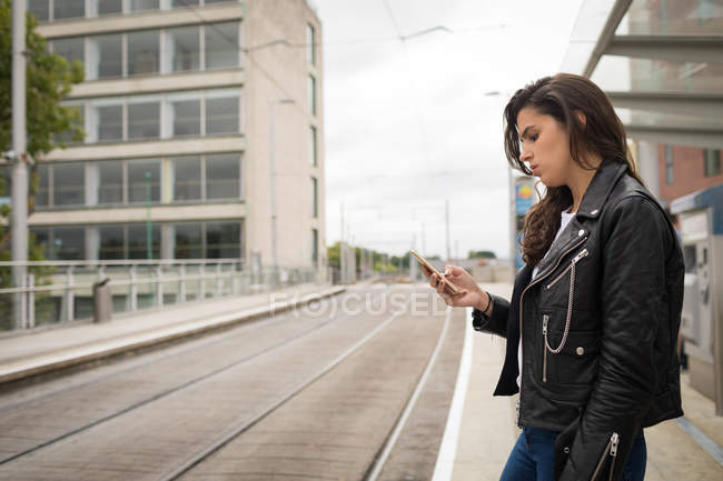 Vista lateral da mulher usando telefone celular na plataforma na estação ferroviária — Fotografia de Stock
