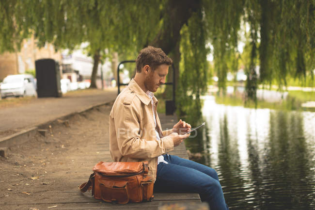 Vista lateral do homem usando tablet digital enquanto sentado perto do lago — Fotografia de Stock