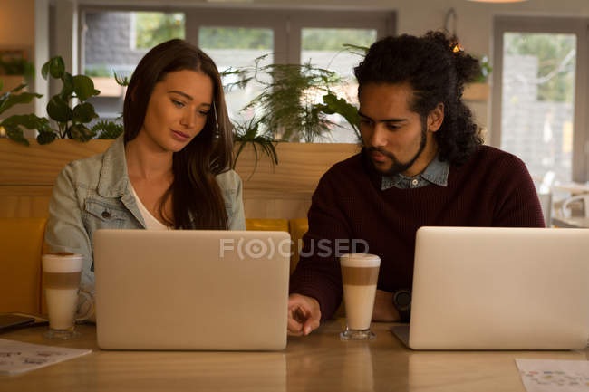 Pareja joven discutiendo sobre portátil en la cafetería - foto de stock