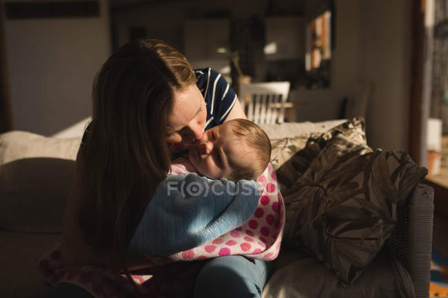 Мама целует своего ребенка на диване дома — стоковое фото