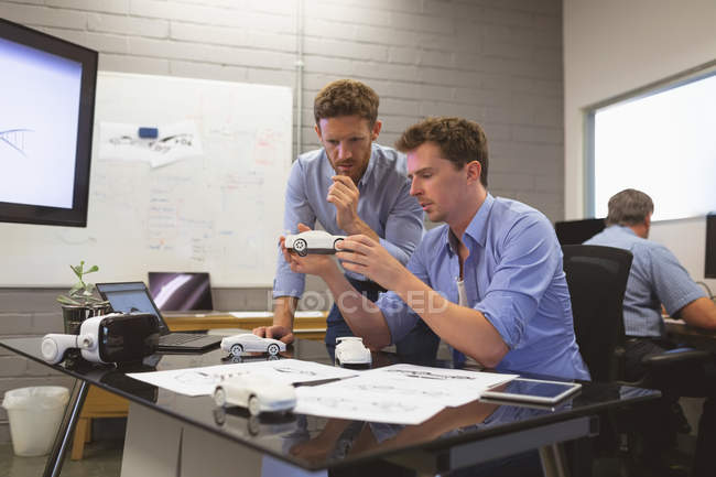 Compañeros de negocios discutiendo sobre modelo de coche en la oficina - foto de stock