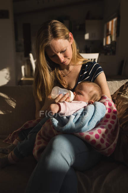 Mother feeding milk to baby on sofa at home — Stock Photo