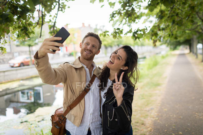Casal feliz tomando selfie perto do lago — Fotografia de Stock
