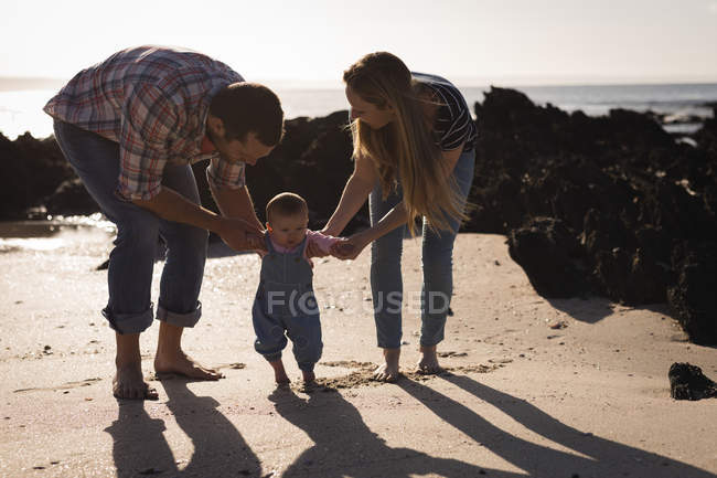 Родители учат ребенка ходить по пляжу в солнечный день — стоковое фото