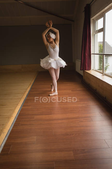 Балерина практикует балет у окна в танцевальной студии — стоковое фото