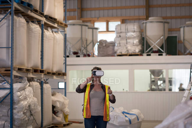 Trabalhadora usando fone de ouvido de realidade virtual no armazém — Fotografia de Stock