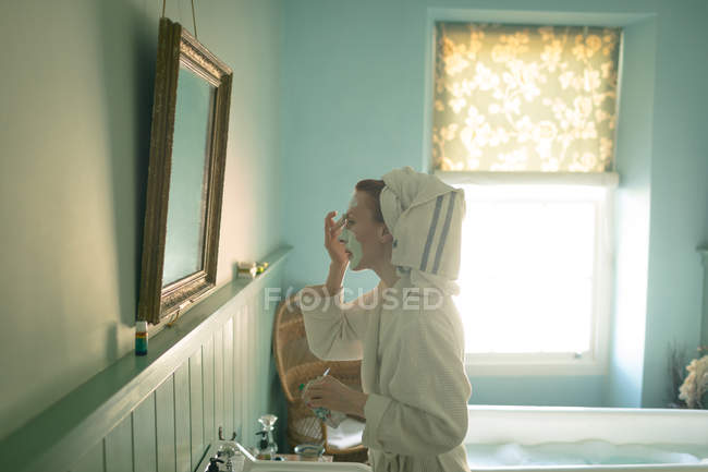 Женщина надевает маску для лица в ванной комнате дома — стоковое фото