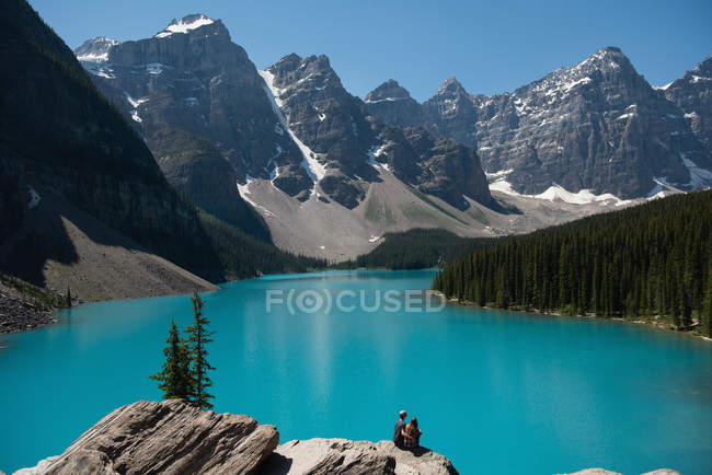 Vue arrière d'un couple assis sur un rocher près d'une rivière — Photo de stock