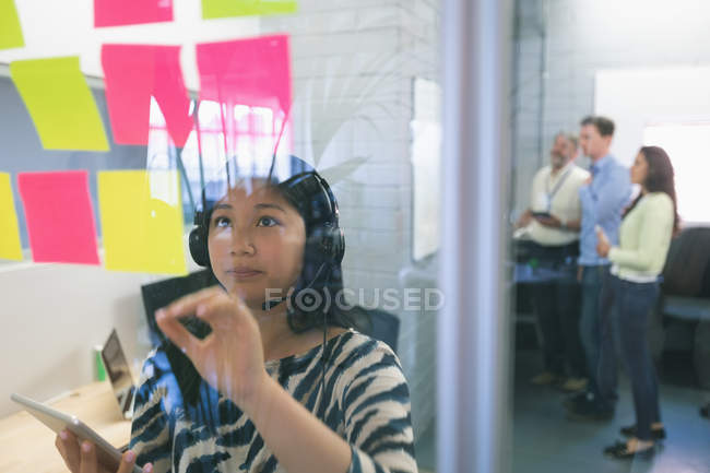 Female executive looking at sticky notes in office — Stock Photo