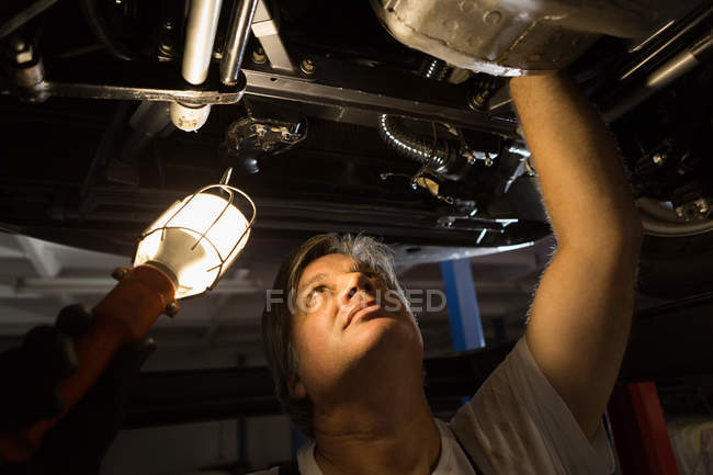 Masculino mecânico examinando um carro na garagem — Fotografia de Stock