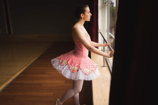 Задумчивая балерина смотрит в окно в танцевальной студии — стоковое фото