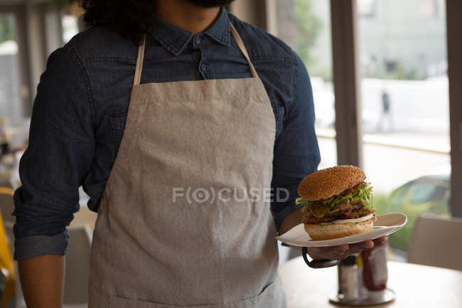 Mid section of waiter holding hamburger in cafe — Stock Photo