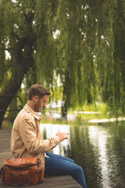 Вид сбоку на человека с помощью цифровой таблички рядом с озером — стоковое фото