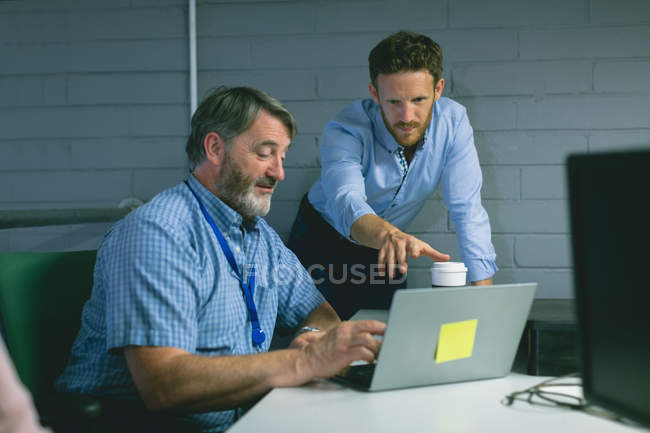 Бізнес-колеги обговорюють ноутбук в офісі — стокове фото