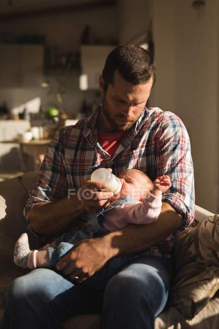 Крупним планом батько годує дитину молоком на дивані вдома — стокове фото