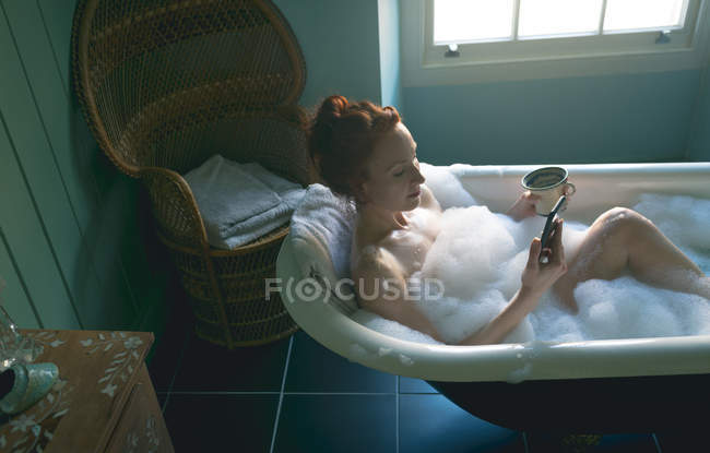 Mulher usando telefone celular na banheira no banheiro — Fotografia de Stock