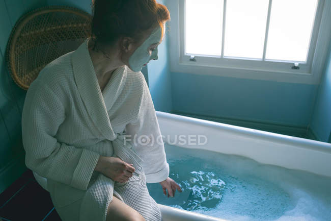Frau sitzt in Badewanne und kontrolliert Wasser im heimischen Badezimmer — Stockfoto