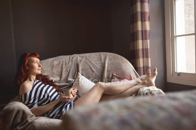 Mulher atenciosa com xícara de café relaxante no sofá em casa — Fotografia de Stock