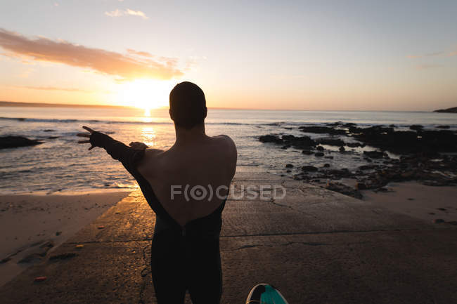 Vista posteriore del surfista che indossa il costume sulla spiaggia durante il tramonto — Foto stock