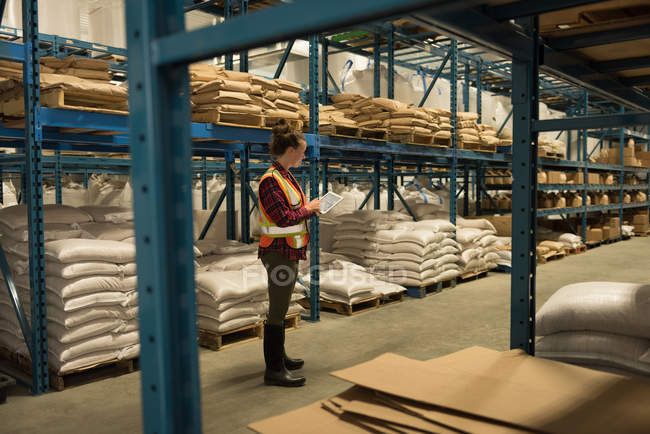 Vue latérale du travailleur féminin utilisant une tablette numérique à l'entrepôt — Photo de stock