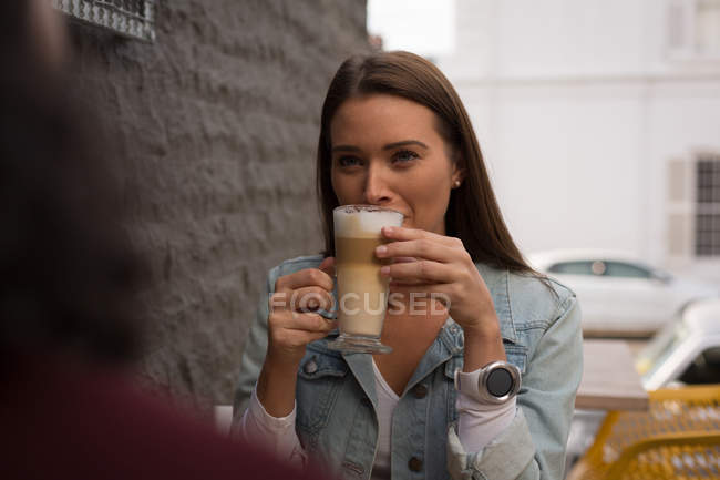 Улыбающаяся женщина пьет кофе в кафе на открытом воздухе — стоковое фото
