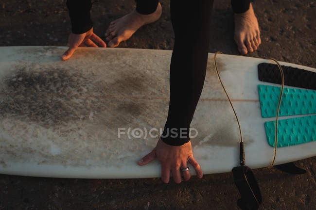 Close-up of surfer picking up surfboard on beach — Stock Photo