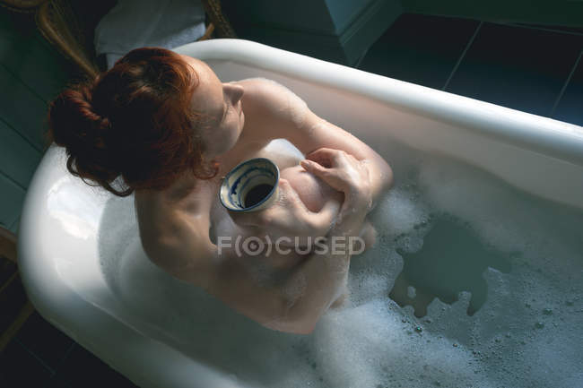 Sobrecarga de la mujer tomando café en la bañera en el baño - foto de stock
