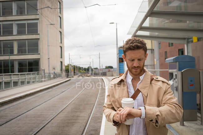 Homem que verifica o tempo no relógio na plataforma na estação ferroviária — Fotografia de Stock