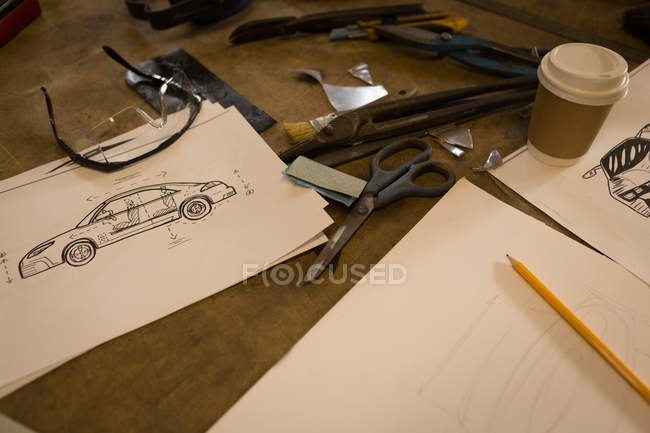 Gráfico, herramientas y taza de café en una mesa en el garaje - foto de stock
