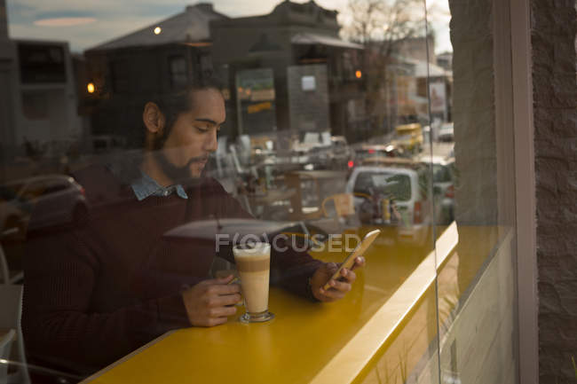 Homem com xícara de café usando telefone celular no café — Fotografia de Stock
