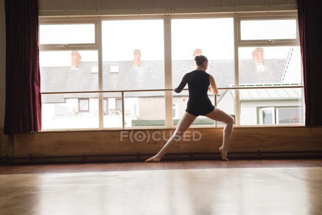 Ballerina stretching on barre while practicing ballet dance in dance studio — Stock Photo