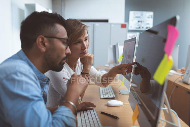 Vista lateral dos executivos discutindo sobre PC desktop na mesa no escritório — Fotografia de Stock