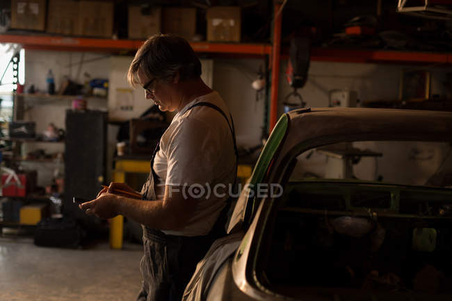 Чоловічий механік з використанням мобільного телефону в гаражі — стокове фото