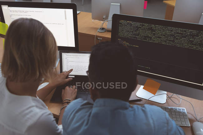 Rear view of executives discussing over laptop at desk in office — Stock Photo