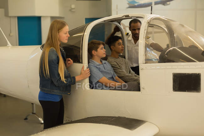 Летчик-мужчина рассказывает детям о самолете в учебном заведении — стоковое фото
