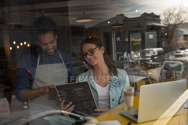 Mulher discutindo cartão de menu com garçom no café — Fotografia de Stock