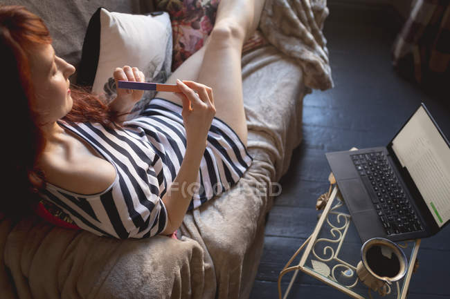 Donna utilizzando lima per unghie sul divano a casa — Foto stock