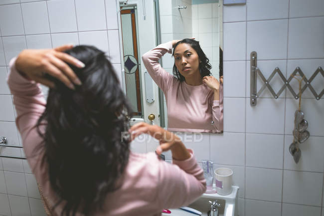 Frau steht mit der Hand an den Haaren im heimischen Badezimmer — Stockfoto