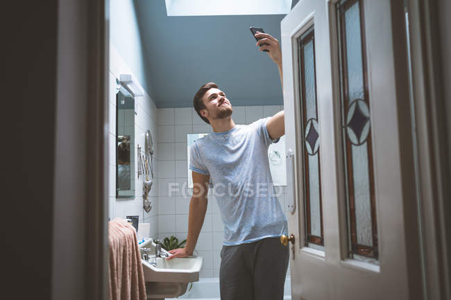Man taking selfie with mobile phone in bedroom at home — Stock Photo